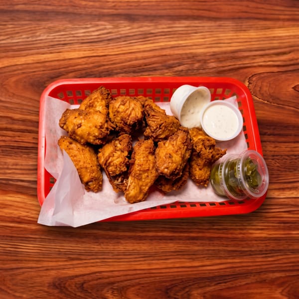 Fried chicken wings in a red basket with ranch and jalapeños on a wooden table.
